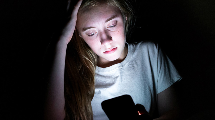adolescent looking at a phone screen, upset, in a dark room