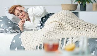 Woman with fever lying in bed checking thermometer