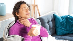 Woman massaging lymph nodes in throat while holding a cup of tea