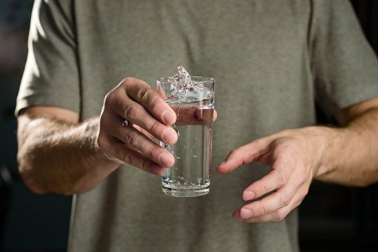 Water splashes from a glass in the hand of a man with tremors