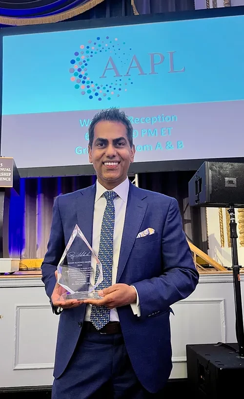 Dr. Sharma holding crystal award in front of large screen