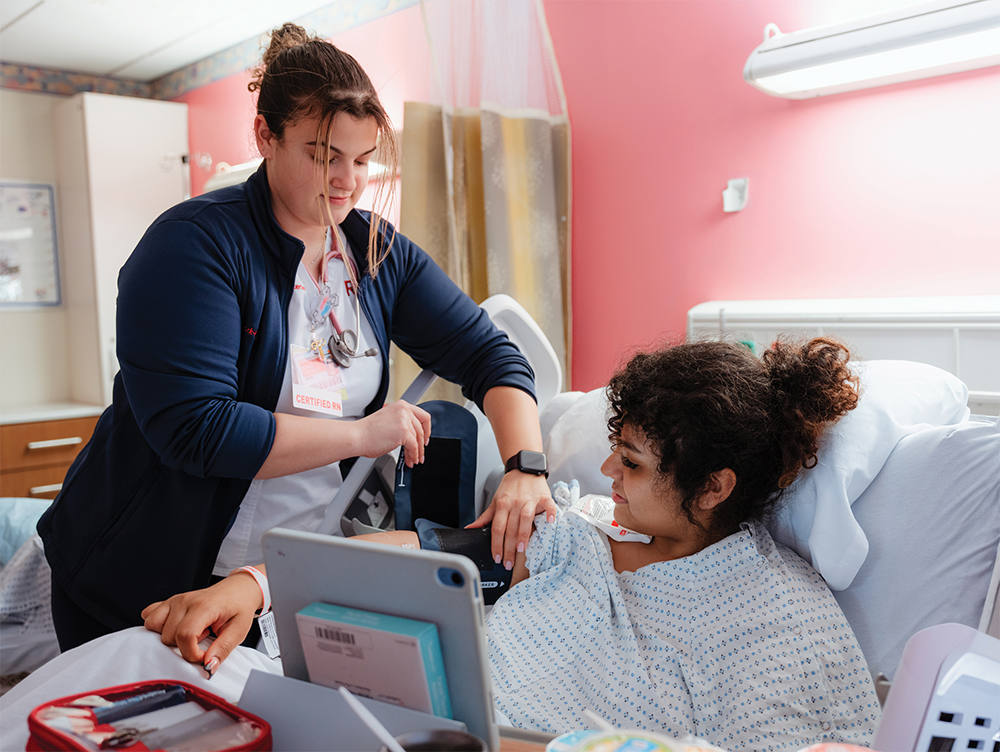 Woman in a hospital bed with a nurse beside it.